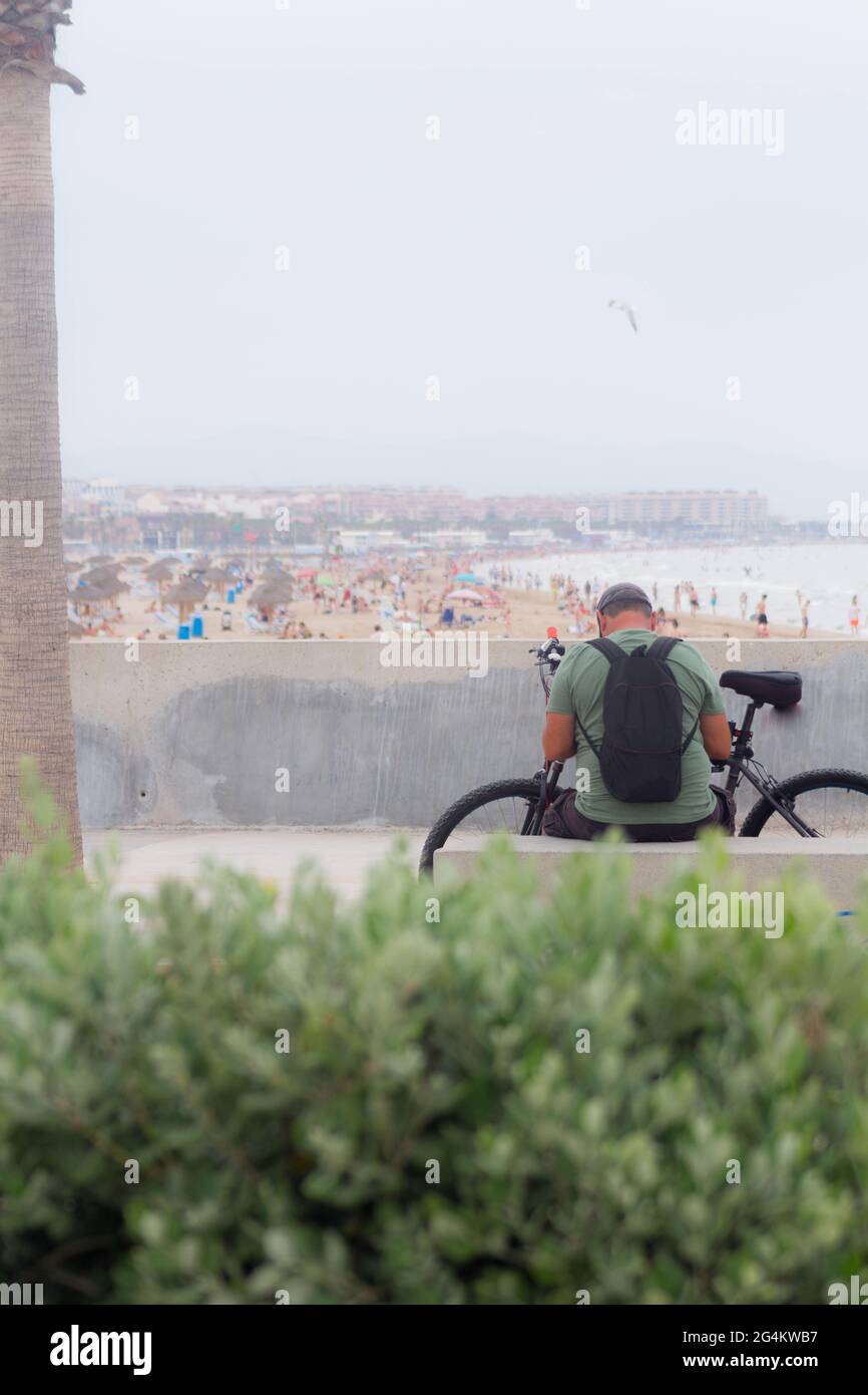 Eine Fahrradtouristin sitzt auf dem Strand und beobachtet den Strand Stockfoto