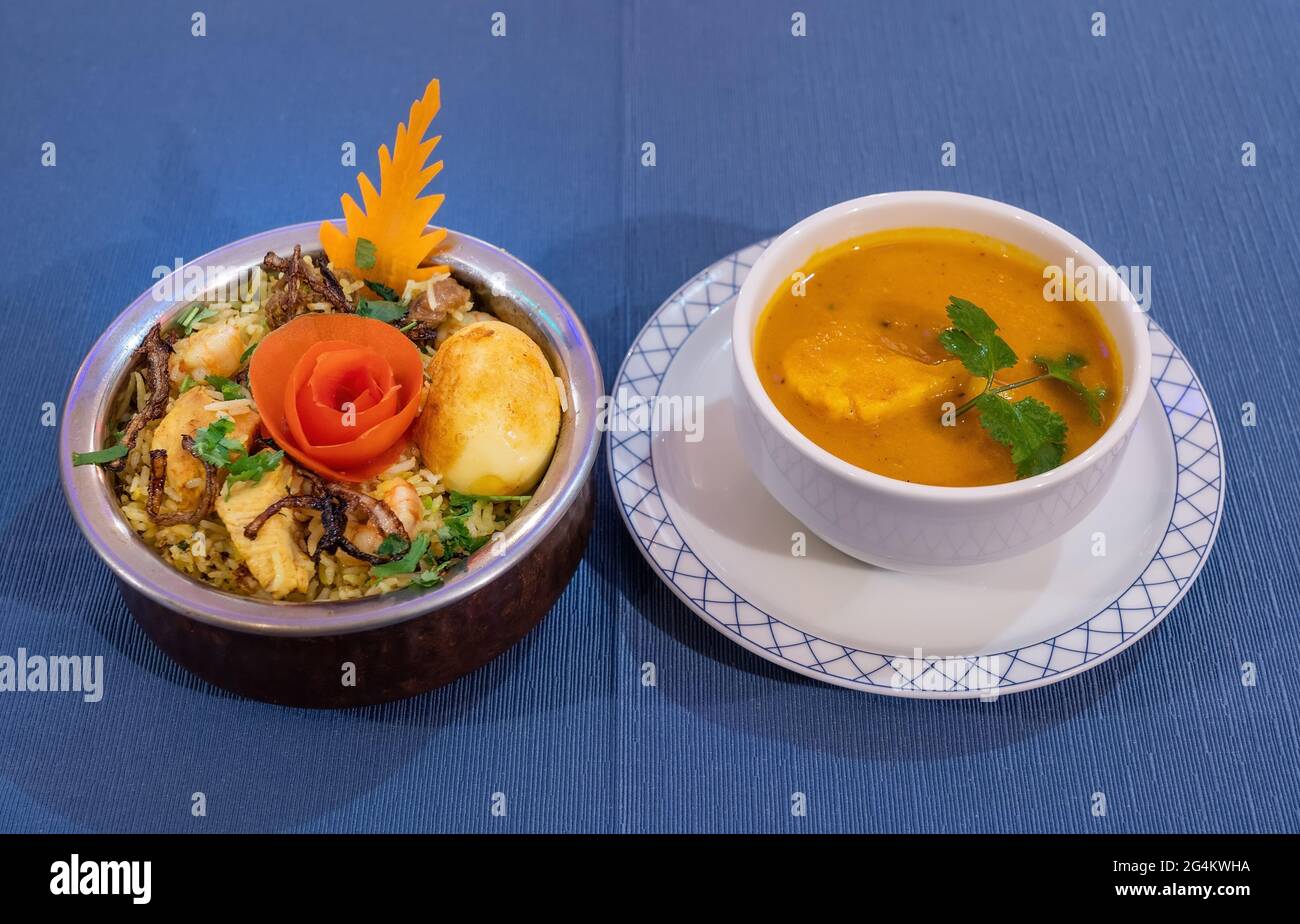 Biryani-Huhn mit Basmati-Reis und Suppe auf blauem Hintergrund. Traditionelle indische Küche. Stockfoto