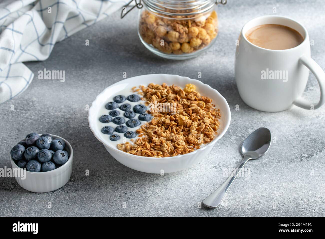 Müsli mit Joghurt und Kaffee auf einem grauen Tisch. Heißer Morgendrink. Müsli und Heidelbeeren in einer weißen Schüssel. Trockenes Frühstückskonzept. Gesund vegetarisch f Stockfoto