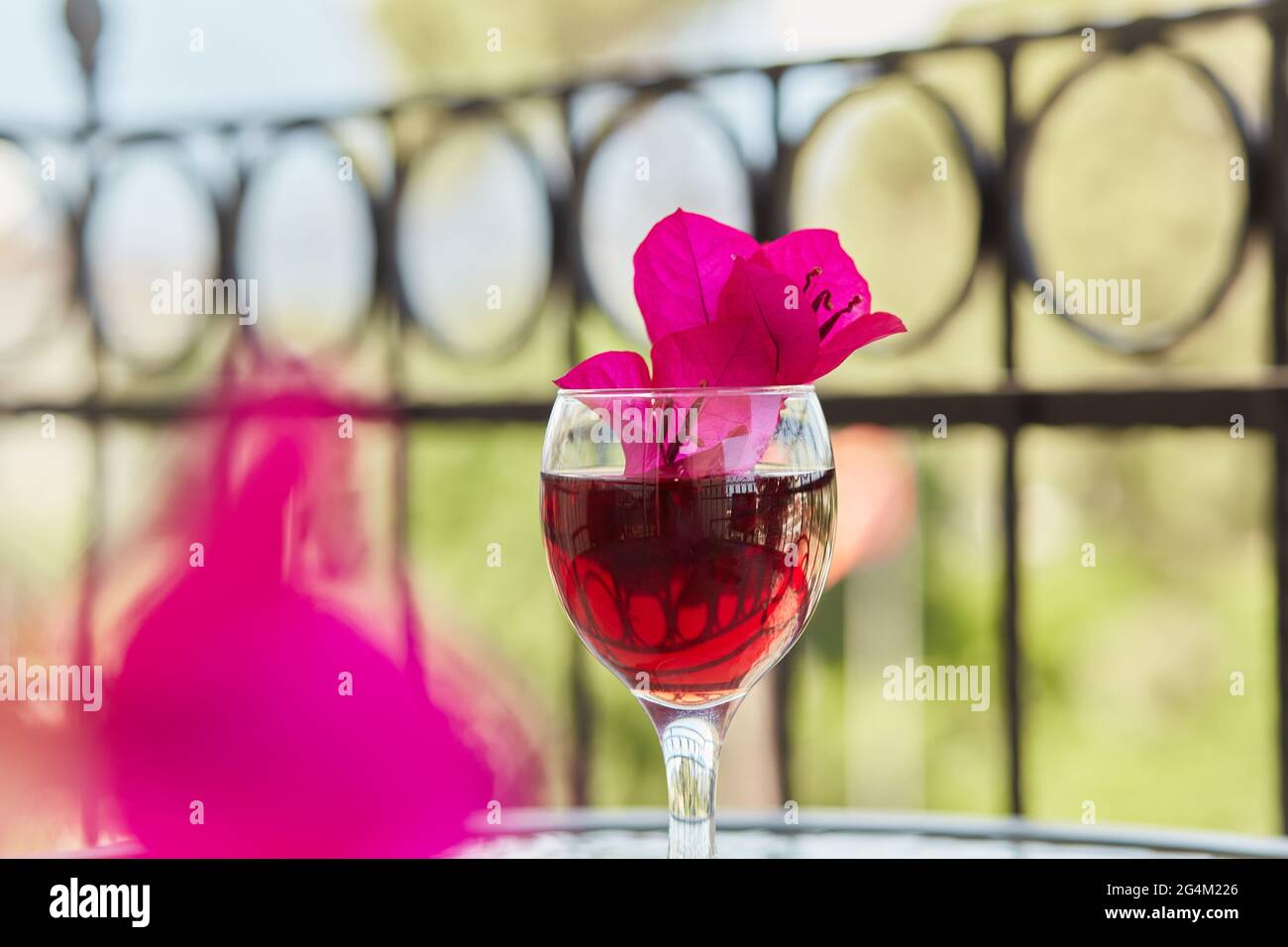 Romantischer Blick auf die Terrasse: Elegantes Glas Rotwein und dekorative rosa Blüten von Bougainvillea in einem Glas im Vordergrund. Festliches Weihnachtskonzept. Kopieren Stockfoto