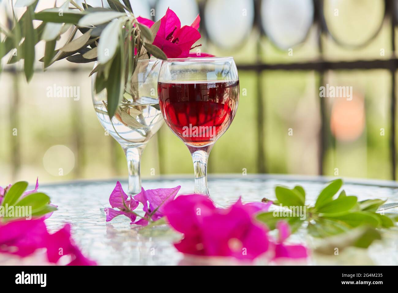 Rosa tropische Blumen und ein Glas Rotwein. Schöner, farbenfroher Sommerhintergrund. Dekorative rosa Blüten von Bougainvillea in einem Glas. Romantisches Abendessen Stockfoto
