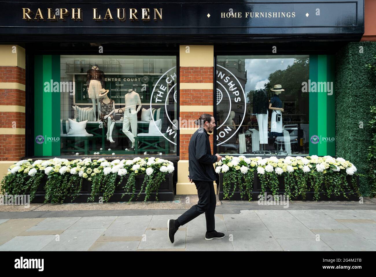 London, Großbritannien. 22. Juni 2021. Ein Mann geht an der Außenfassade des Ralph Lauren-Ladens am Sloane Square vorbei, der vor den kommenden Wimbledon-Tennismeisterschaften im All England Club dekoriert wurde. Ralph Lauren liefert den Beamten bei der Veranstaltung Outfits. Lockdown-Beschränkungen werden die Menge begrenzen, aber das Finale wird voll ausgelastet sein, wenn die Einschränkungen gelockert werden. Kredit: Stephen Chung / Alamy Live Nachrichten Stockfoto