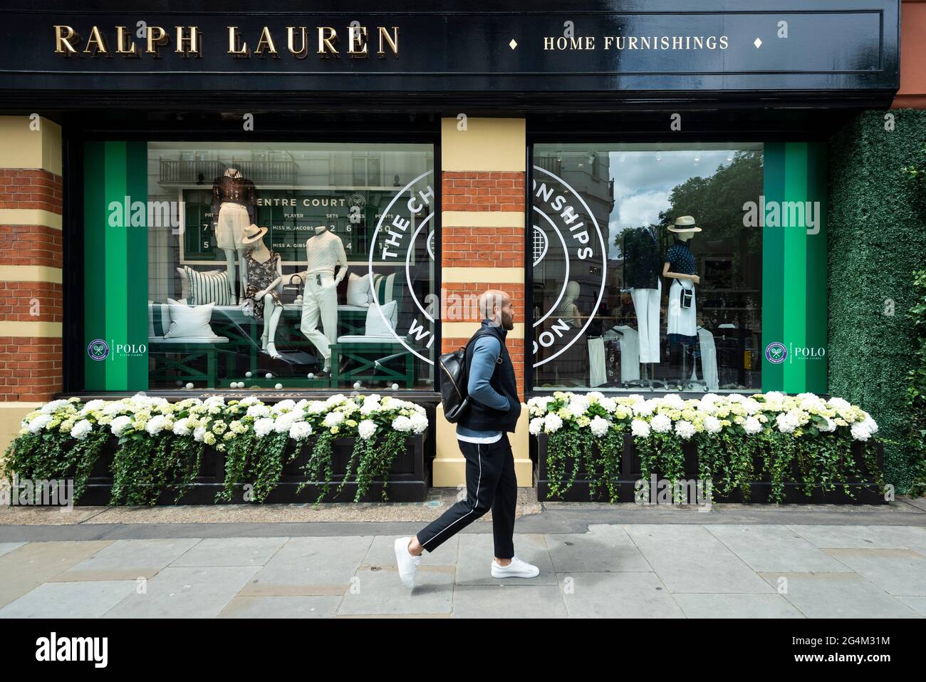 London, Großbritannien. 22. Juni 2021. Ein Mann geht an der Außenfassade des Ralph Lauren-Ladens am Sloane Square vorbei, der vor den kommenden Wimbledon-Tennismeisterschaften im All England Club dekoriert wurde. Ralph Lauren liefert den Beamten bei der Veranstaltung Outfits. Lockdown-Beschränkungen werden die Menge begrenzen, aber das Finale wird voll ausgelastet sein, wenn die Einschränkungen gelockert werden. Kredit: Stephen Chung / Alamy Live Nachrichten Stockfoto