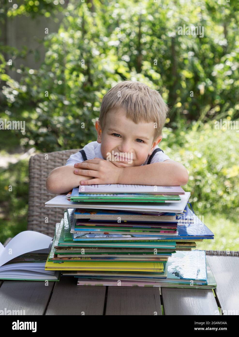 Der Vorschulkinder sitzt am Tisch, vor ihm ist ein großer Haufen von Kinderbüchern, vor einem grünen Hintergrund. Bücher lesen, Kinderfantasien, ich Stockfoto