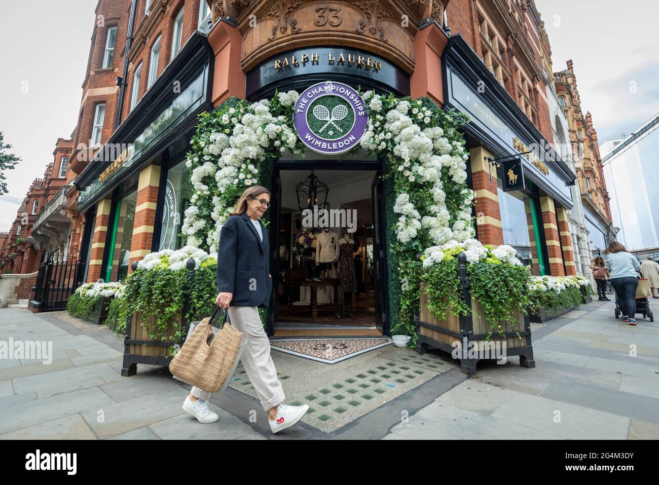 London, Großbritannien. 22. Juni 2021. Eine Frau geht an der Außenfassade des Ralph Lauren-Ladens am Sloane Square vorbei, der vor den kommenden Wimbledon-Tennismeisterschaften im All England Club dekoriert wurde. Ralph Lauren liefert den Beamten bei der Veranstaltung Outfits. Lockdown-Beschränkungen werden die Menge begrenzen, aber das Finale wird voll ausgelastet sein, wenn die Einschränkungen gelockert werden. Kredit: Stephen Chung / Alamy Live Nachrichten Stockfoto