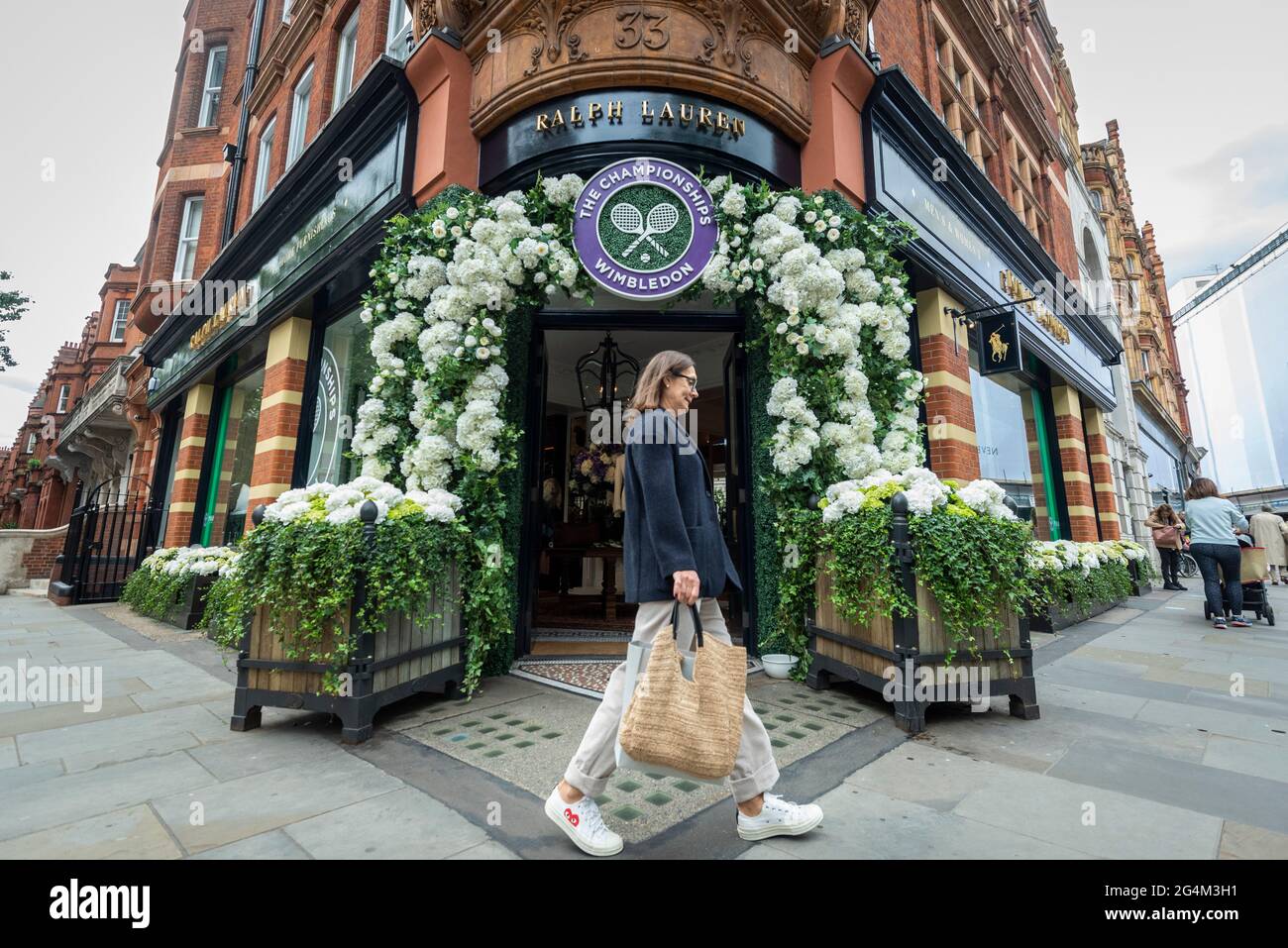 London, Großbritannien. 22. Juni 2021. Eine Frau geht an der Außenfassade des Ralph Lauren-Ladens am Sloane Square vorbei, der vor den kommenden Wimbledon-Tennismeisterschaften im All England Club dekoriert wurde. Ralph Lauren liefert den Beamten bei der Veranstaltung Outfits. Lockdown-Beschränkungen werden die Menge begrenzen, aber das Finale wird voll ausgelastet sein, wenn die Einschränkungen gelockert werden. Kredit: Stephen Chung / Alamy Live Nachrichten Stockfoto