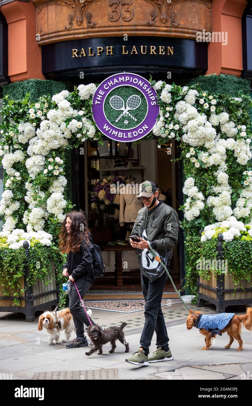 London, Großbritannien. 22. Juni 2021. Dogwalkers passieren die Außenfassade des Ralph Lauren-Ladens am Sloane Square, der vor den kommenden Wimbledon-Tennismeisterschaften im All England Club eingerichtet wurde. Ralph Lauren liefert den Beamten bei der Veranstaltung Outfits. Lockdown-Beschränkungen werden die Menge begrenzen, aber das Finale wird voll ausgelastet sein, wenn die Einschränkungen gelockert werden. Kredit: Stephen Chung / Alamy Live Nachrichten Stockfoto