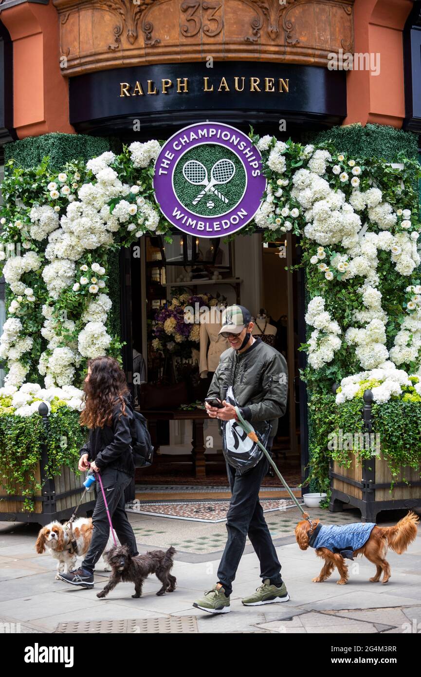 London, Großbritannien. 22. Juni 2021. Dogwalkers passieren die Außenfassade des Ralph Lauren-Ladens am Sloane Square, der vor den kommenden Wimbledon-Tennismeisterschaften im All England Club eingerichtet wurde. Ralph Lauren liefert den Beamten bei der Veranstaltung Outfits. Lockdown-Beschränkungen werden die Menge begrenzen, aber das Finale wird voll ausgelastet sein, wenn die Einschränkungen gelockert werden. Kredit: Stephen Chung / Alamy Live Nachrichten Stockfoto