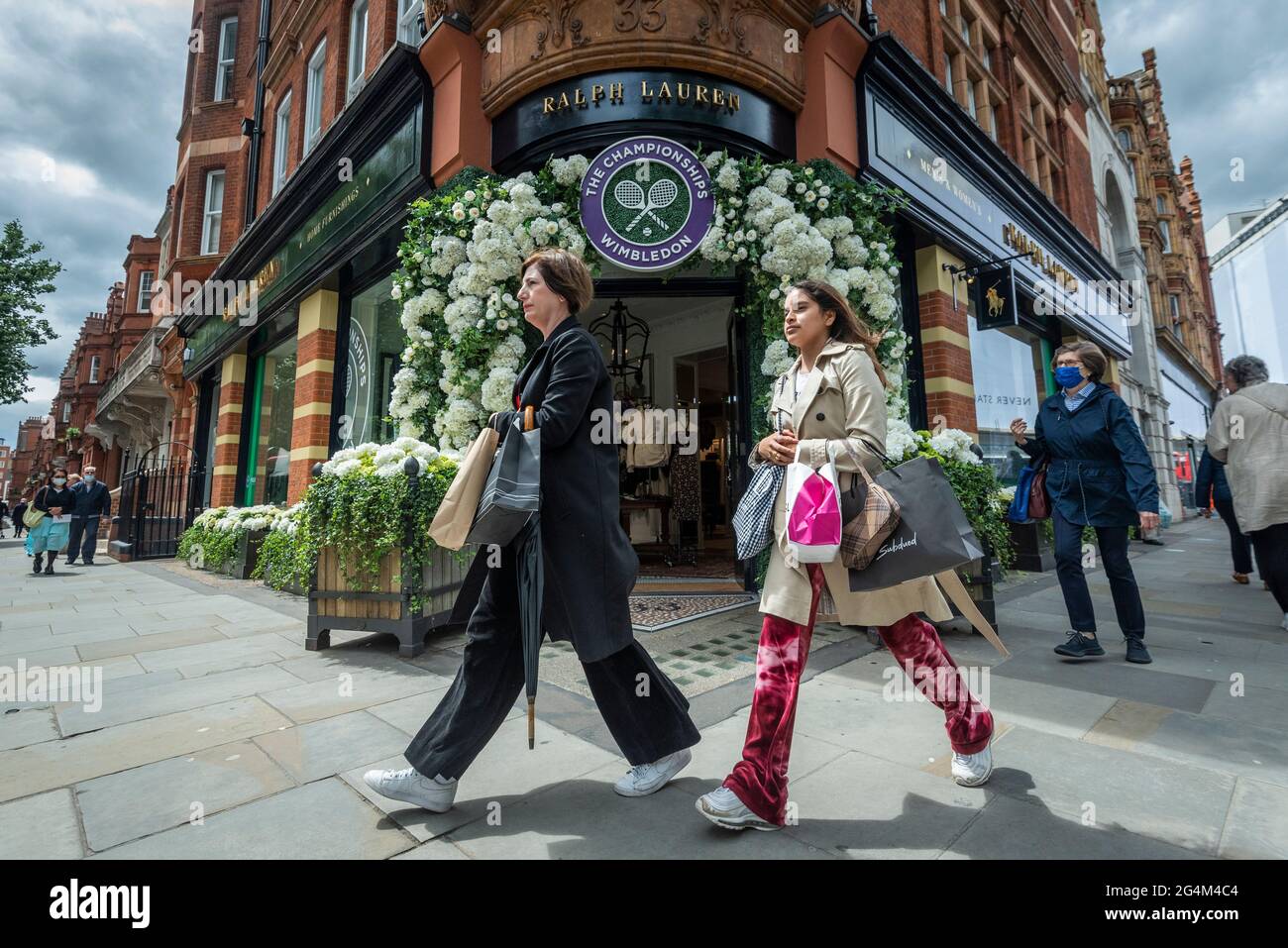 London, Großbritannien. 22. Juni 2021. Die Frauen gehen an der Außenseite des Ralph Lauren-Ladens am Sloane Square vorbei, der vor den kommenden Wimbledon-Tennismeisterschaften im All England Club dekoriert wurde. Ralph Lauren liefert den Beamten bei der Veranstaltung Outfits. Lockdown-Beschränkungen werden die Menge begrenzen, aber das Finale wird voll ausgelastet sein, wenn die Einschränkungen gelockert werden. Kredit: Stephen Chung / Alamy Live Nachrichten Stockfoto