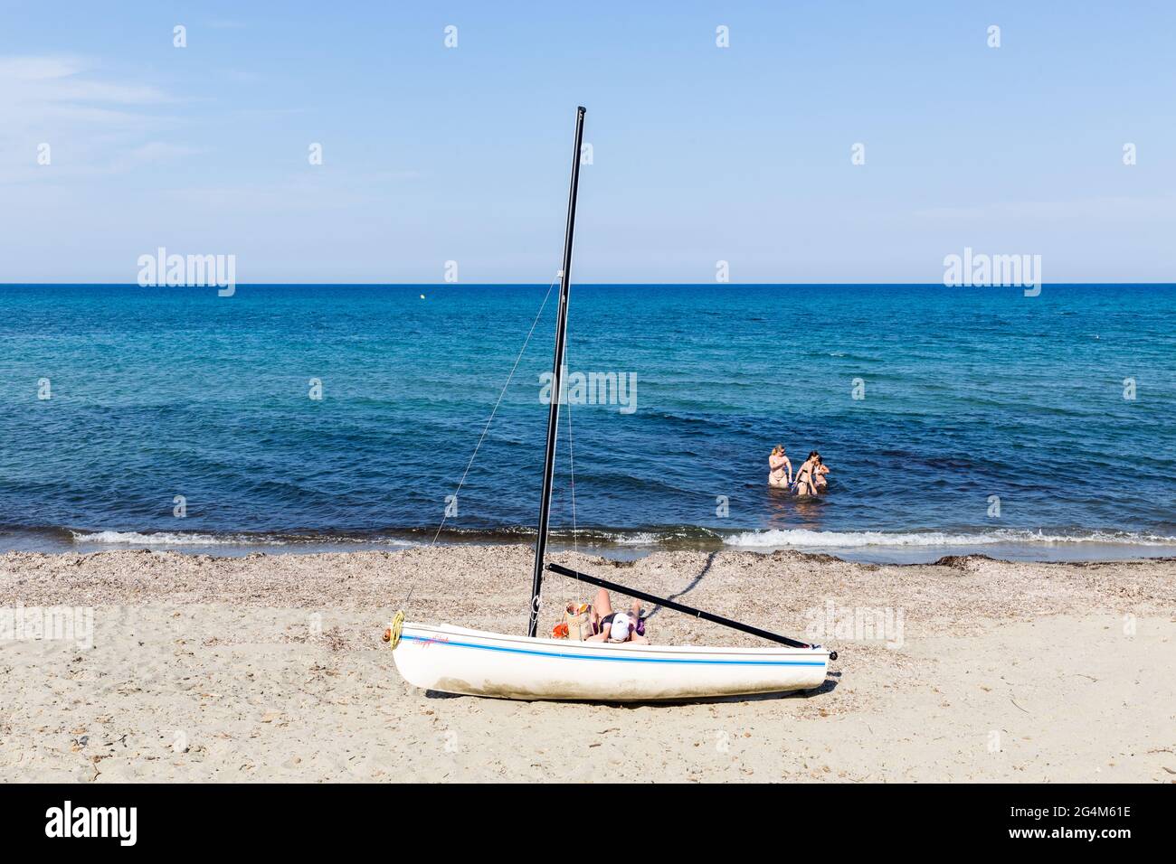Segelboot am Strand gestrandet; eine Person bräunend; drei Personen baden. Prunete Beach, Korsika, Frankreich Stockfoto