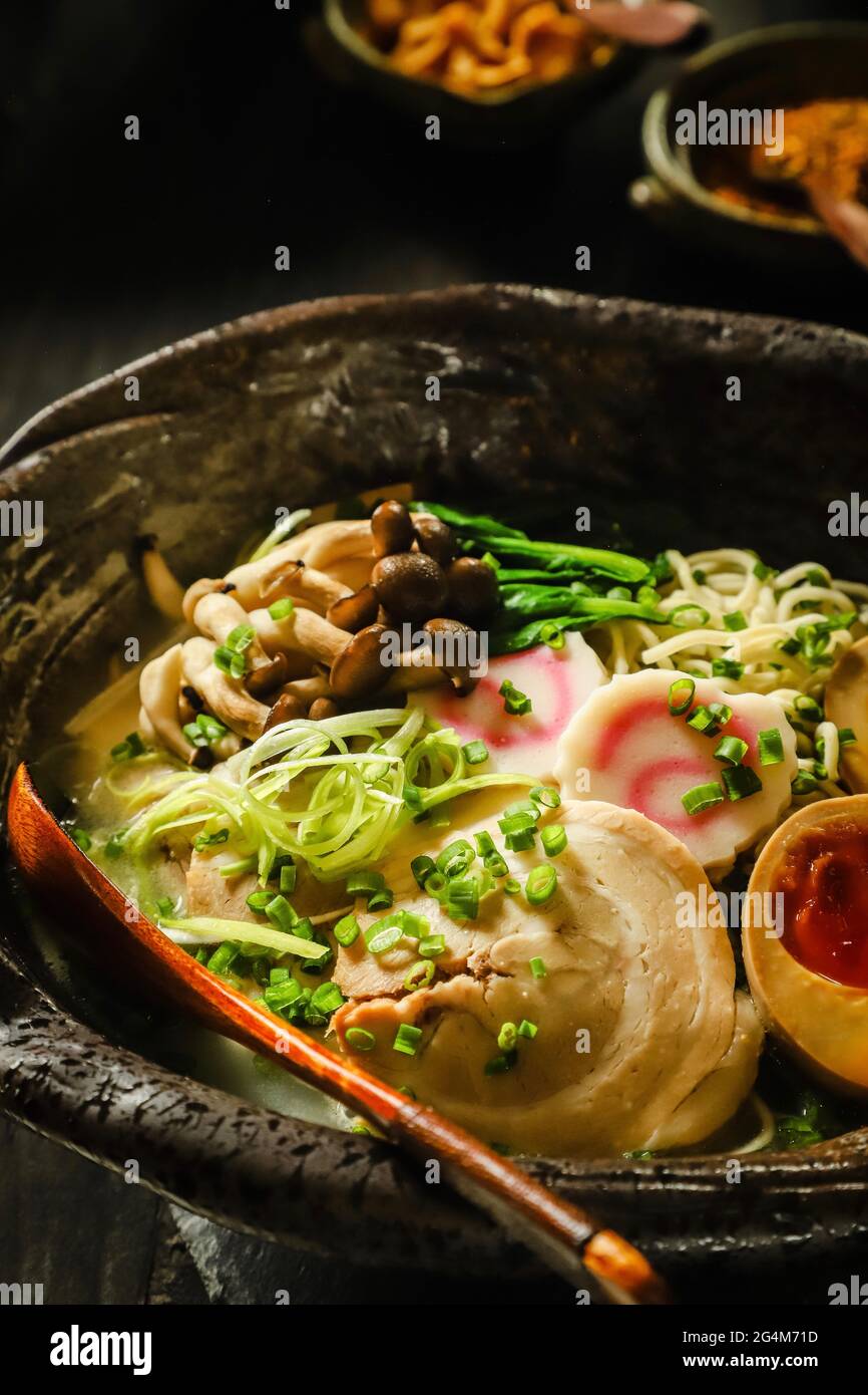 Ramen. Japanische gelbe Nudelsuppe mit Schweinebauch, Soja-Ei, Fischkuchen, Pilzen und grünem Gemüse. Stockfoto