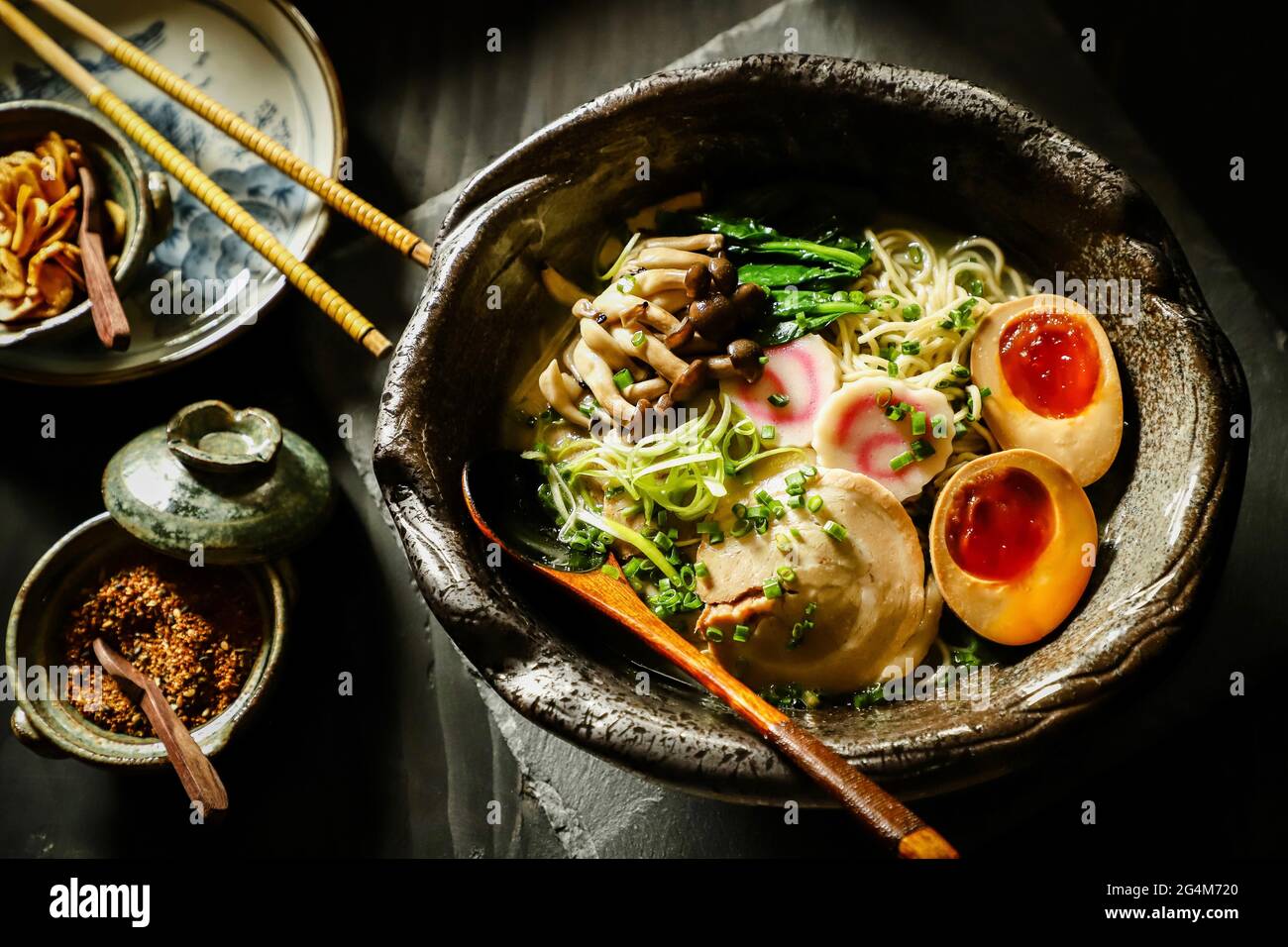 Ramen. Japanische gelbe Nudelsuppe mit Schweinebauch, Soja-Ei, Fischkuchen, Pilzen und grünem Gemüse. Stockfoto