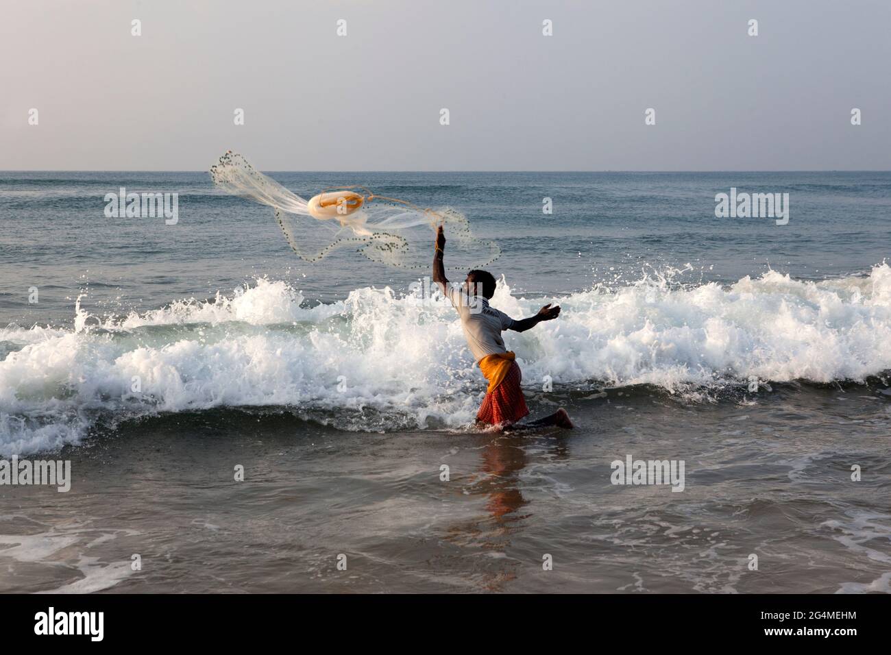 Ein Fischer, der versucht, Fische zu fangen, indem er ein Netz in das wellige Meer bei Puri wirft, einem berühmten Touristenstrand im Osten Indiens. Stockfoto