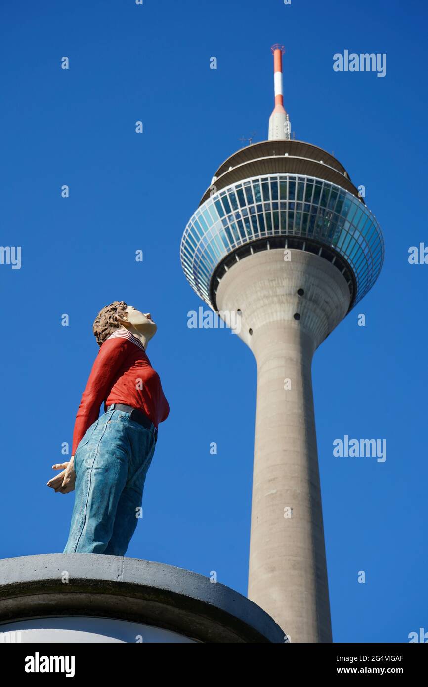 Selektiver Fokus auf 'Marlis', einer lebensgroßen Skulptur des Künstlers Christoph Pöggeler. Sie scheint das Wahrzeichen Düsseldorfs, den Rheinturm, zu betrachten. Stockfoto