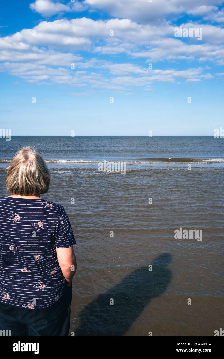 Eine blonde Frau genießt es, das Meer zu beobachten, während die Wellen an einem schönen sonnigen Tag in Großbritannien zum Strand Rollen Stockfoto