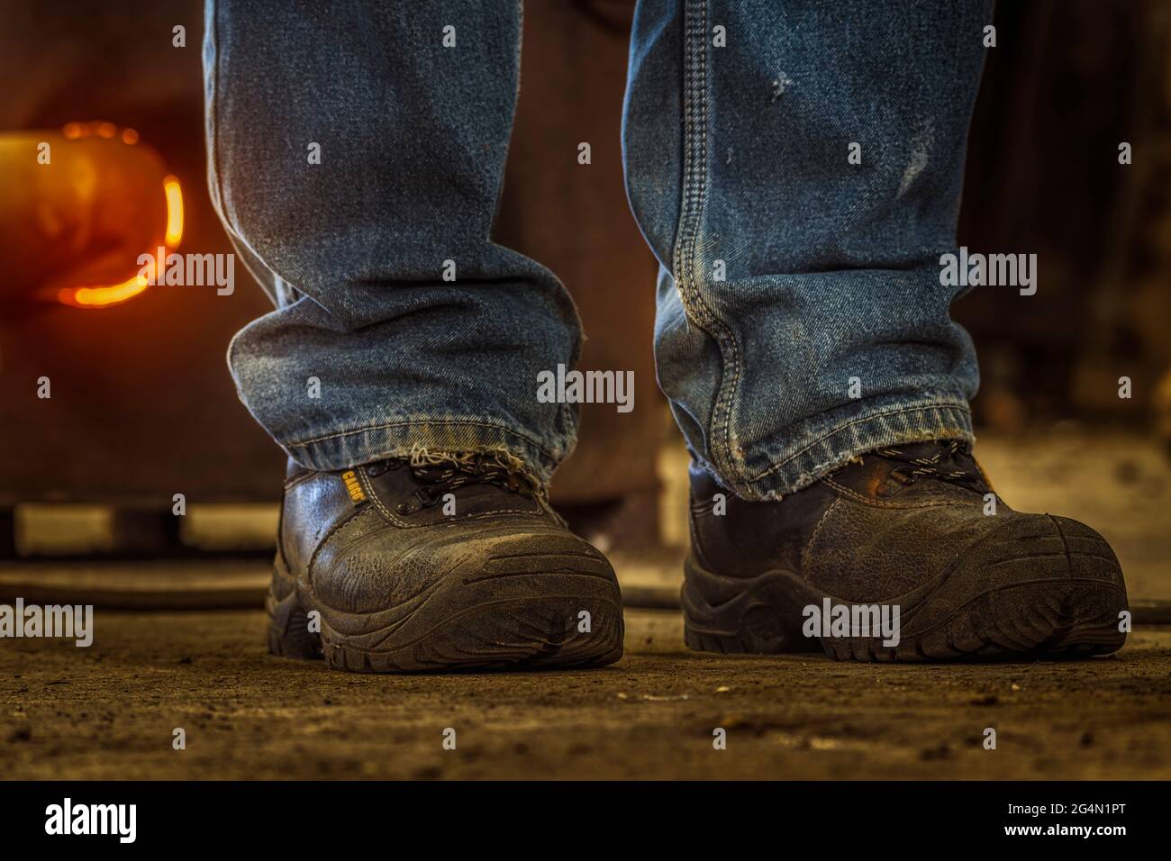 Arbeitskonzept. Nahaufnahme von Herrenjeans und Arbeitsstiefeln mit einem heißen Ofen im Hintergrund. Stockfoto