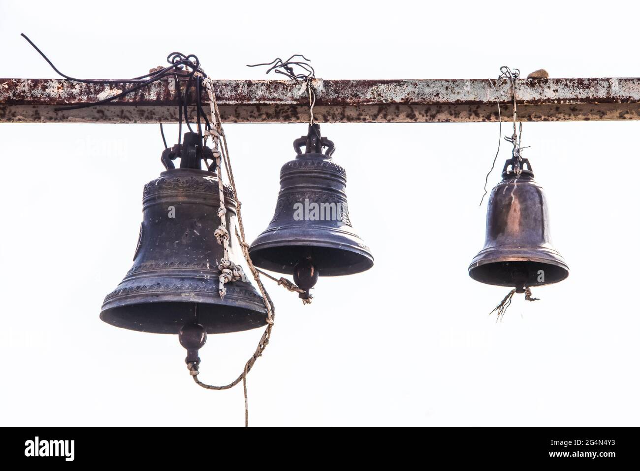 Alte gegossene Glocken, die an einem grungigen rostigen Metallträger in einem orthodoxen Kloster in Osteuropa hängen Stockfoto