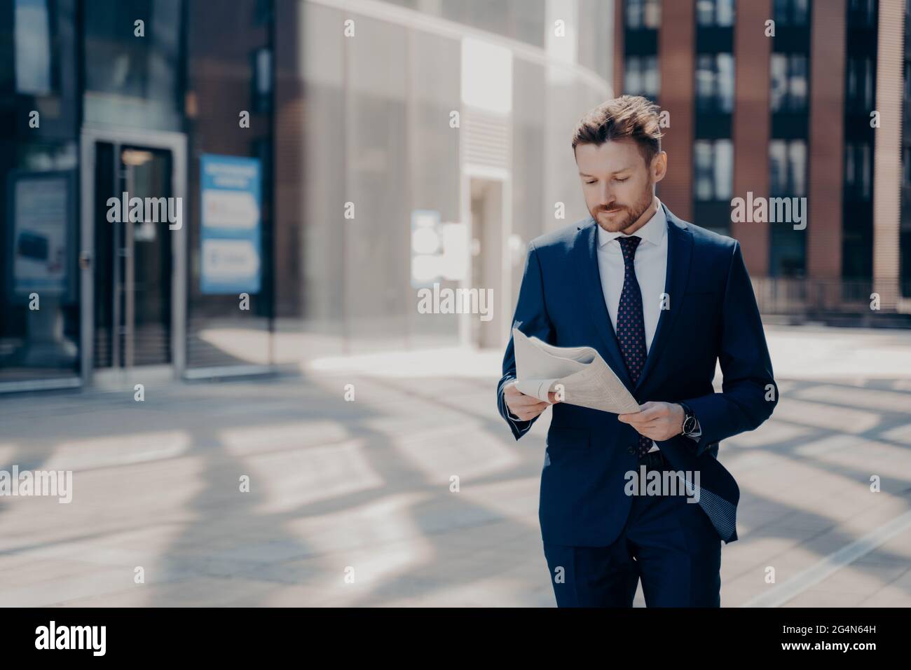 Erfolgreicher Geschäftsmann in formeller Kleidung liest Zeitung beim Gehen Stockfoto