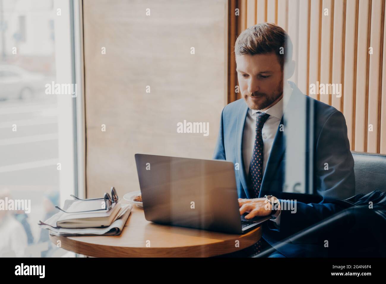 Ein junger, gutaussehender Geschäftsmann mit gepflegtem Bart sitzt am Tisch im Café mit Laptop Stockfoto