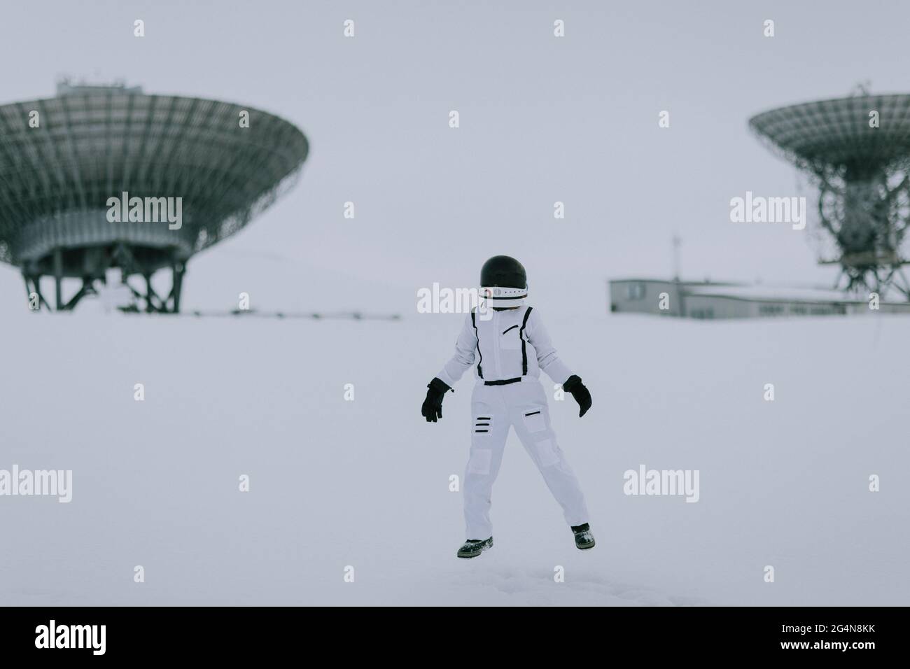 Nicht erkennbarer Kosmonaut im Raumanzügen, der im Winter im verschneiten Tal auf dem Hintergrund riesiger Radarantennen in Spitzbergen steht Stockfoto