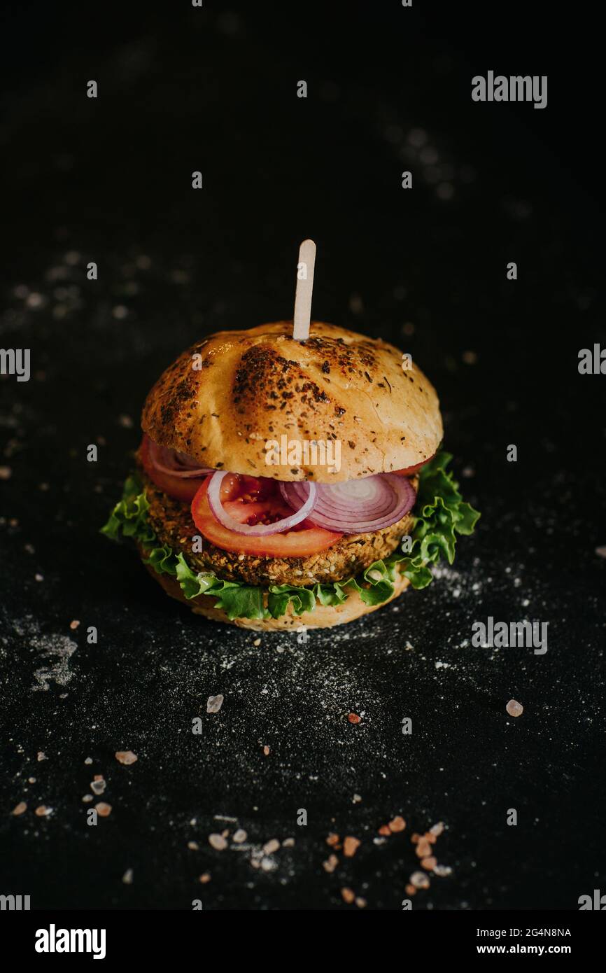 Leckerer veganer Burger mit frischem, reifen Gemüse, serviert auf schwarzem Hintergrund im Studio Stockfoto