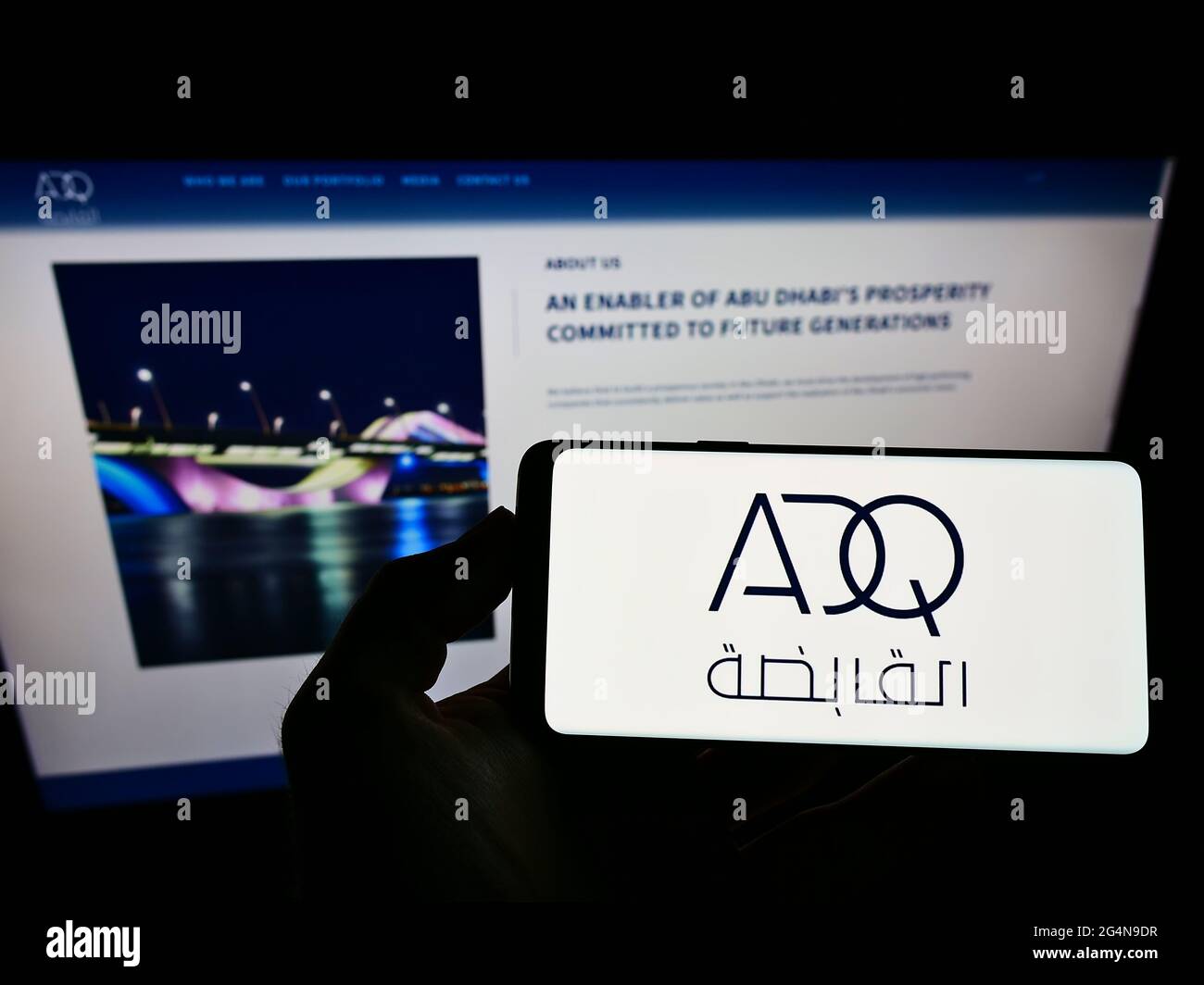 Person, die das Smartphone mit dem Logo der Abu Dhabi Developmental Holding Company (ADQ) auf dem Bildschirm vor der Website hält. Konzentrieren Sie sich auf die Telefonanzeige. Stockfoto