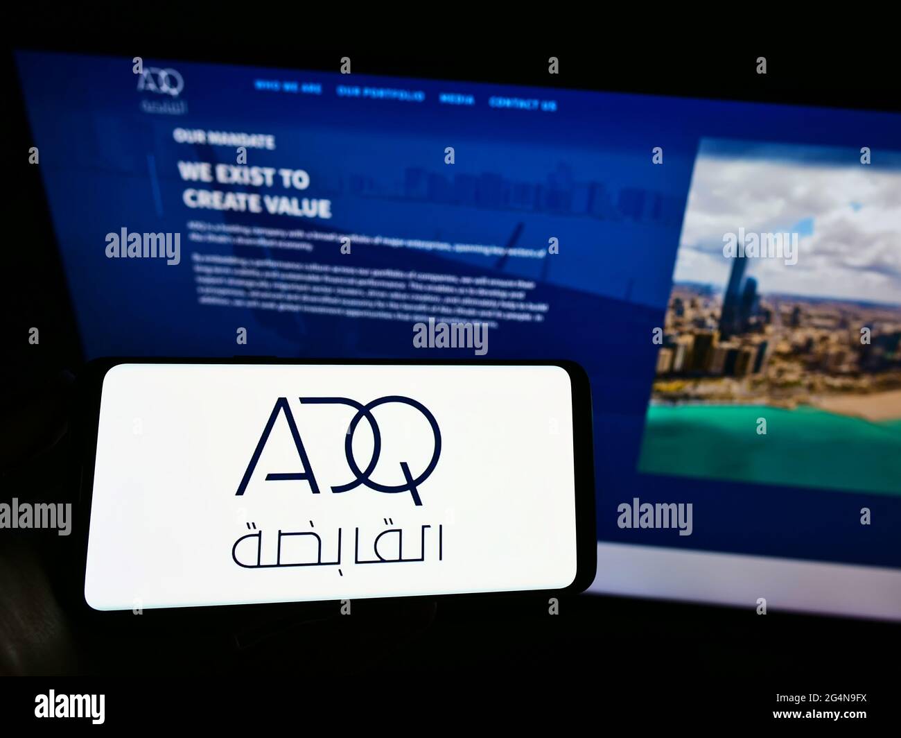 Person mit Mobiltelefon und Logo der Abu Dhabi Developmental Holding Company (ADQ) auf dem Bildschirm vor der Webseite. Konzentrieren Sie sich auf die Telefonanzeige. Stockfoto
