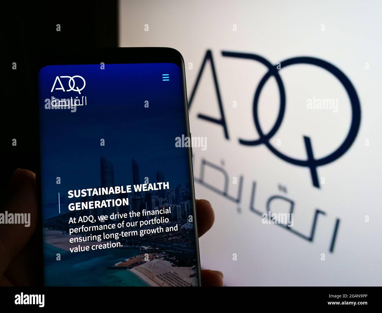 Person, die Mobiltelefon mit Website der Firma Abu Dhabi Developmental Holding Company (ADQ) auf dem Bildschirm mit Logo hält. Konzentrieren Sie sich auf die Mitte des Telefondisplays. Stockfoto