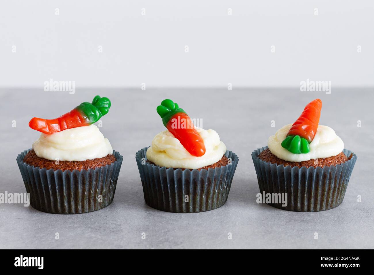 Reihen von süßen, köstlichen Karotten-Cupcakes mit zartem Creme und karottenförmigen Gummitüffeln auf grauer Oberfläche Stockfoto