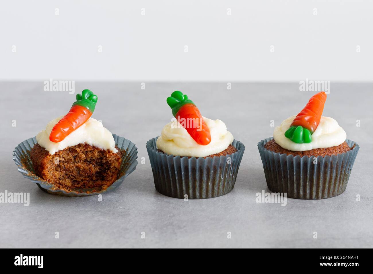 Reihen von süßen, köstlichen Karotten-Cupcakes mit zartem Creme und karottenförmigen Gummitüffeln auf grauer Oberfläche Stockfoto