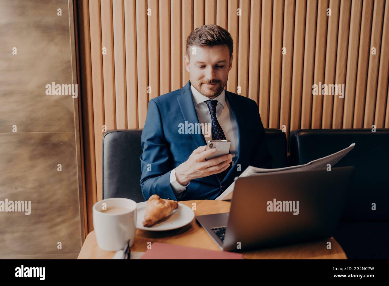 Selbstbewusster junger Geschäftsmann in formeller Kleidung, der Kaffee genießt und fernab im Café arbeitet Stockfoto