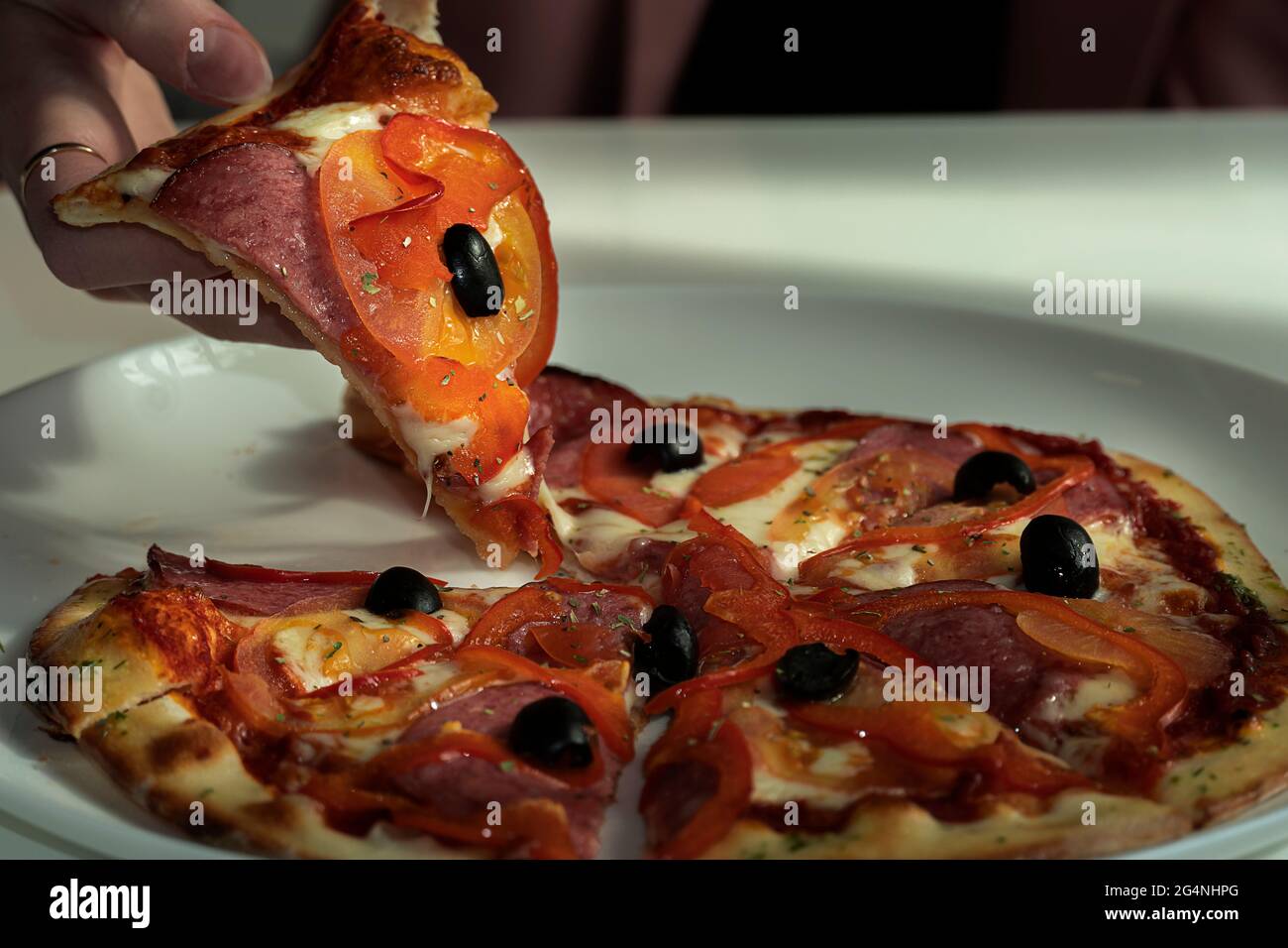Weibliche Hand nimmt eine Scheibe Pizza mit Mozzarella-Käse, Schinken und Ananas. Italienische Pizza auf Holztisch Hintergrund Stockfoto