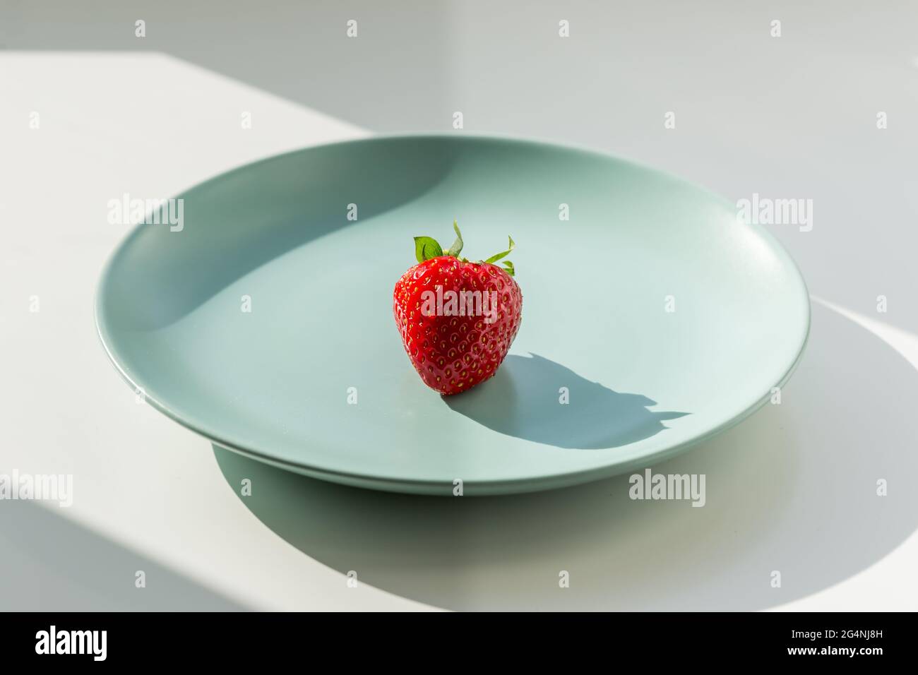 Eine rote Erdbeere auf dem grünen Teller. Gesundes Lifestyle-Konzept. Stockfoto