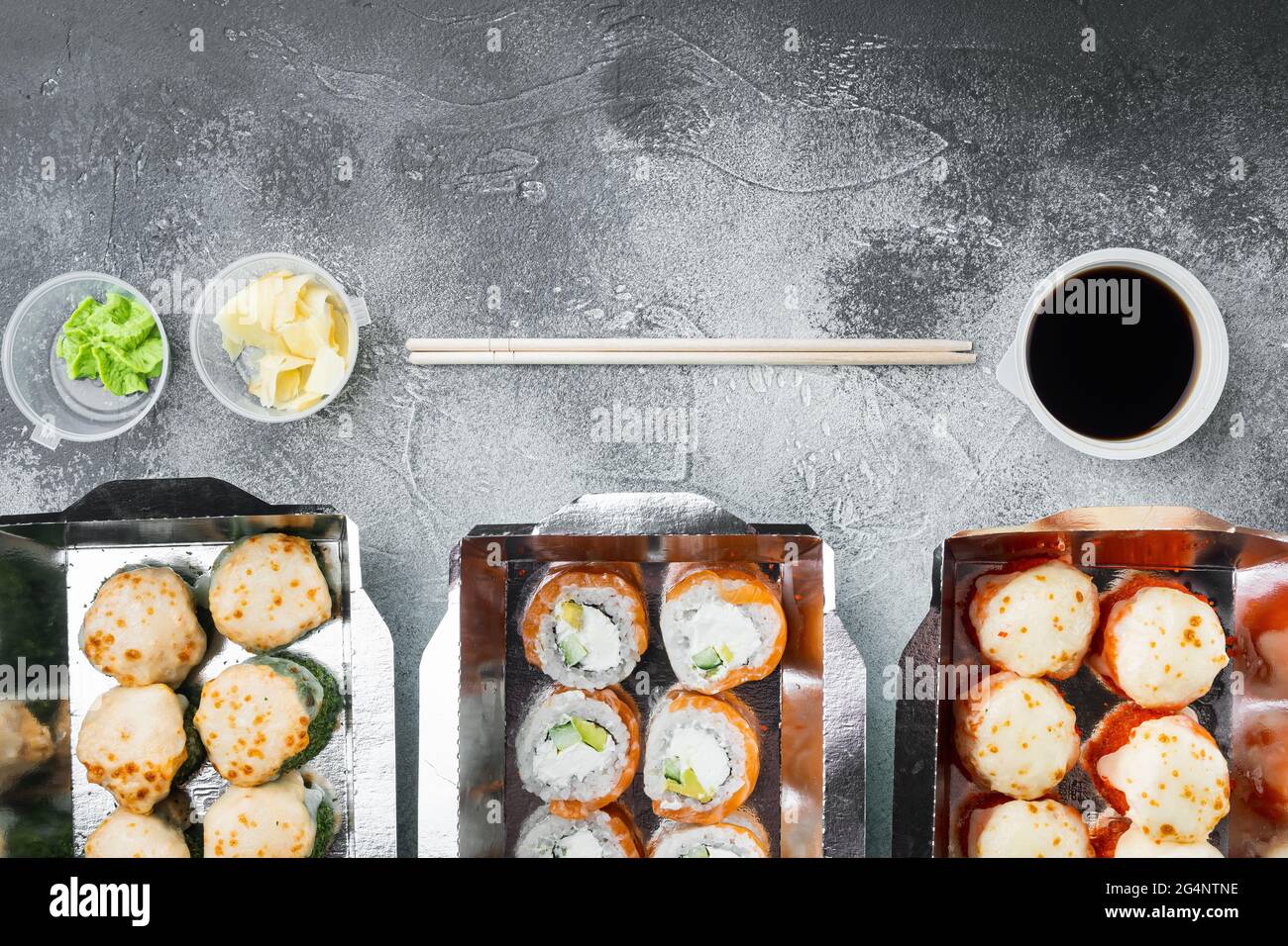 Sushi-Rollen im Take-away-Container-Set, auf grauem Steinhintergrund, Draufsicht flach liegend, mit Copyspace und Platz für Text Stockfoto