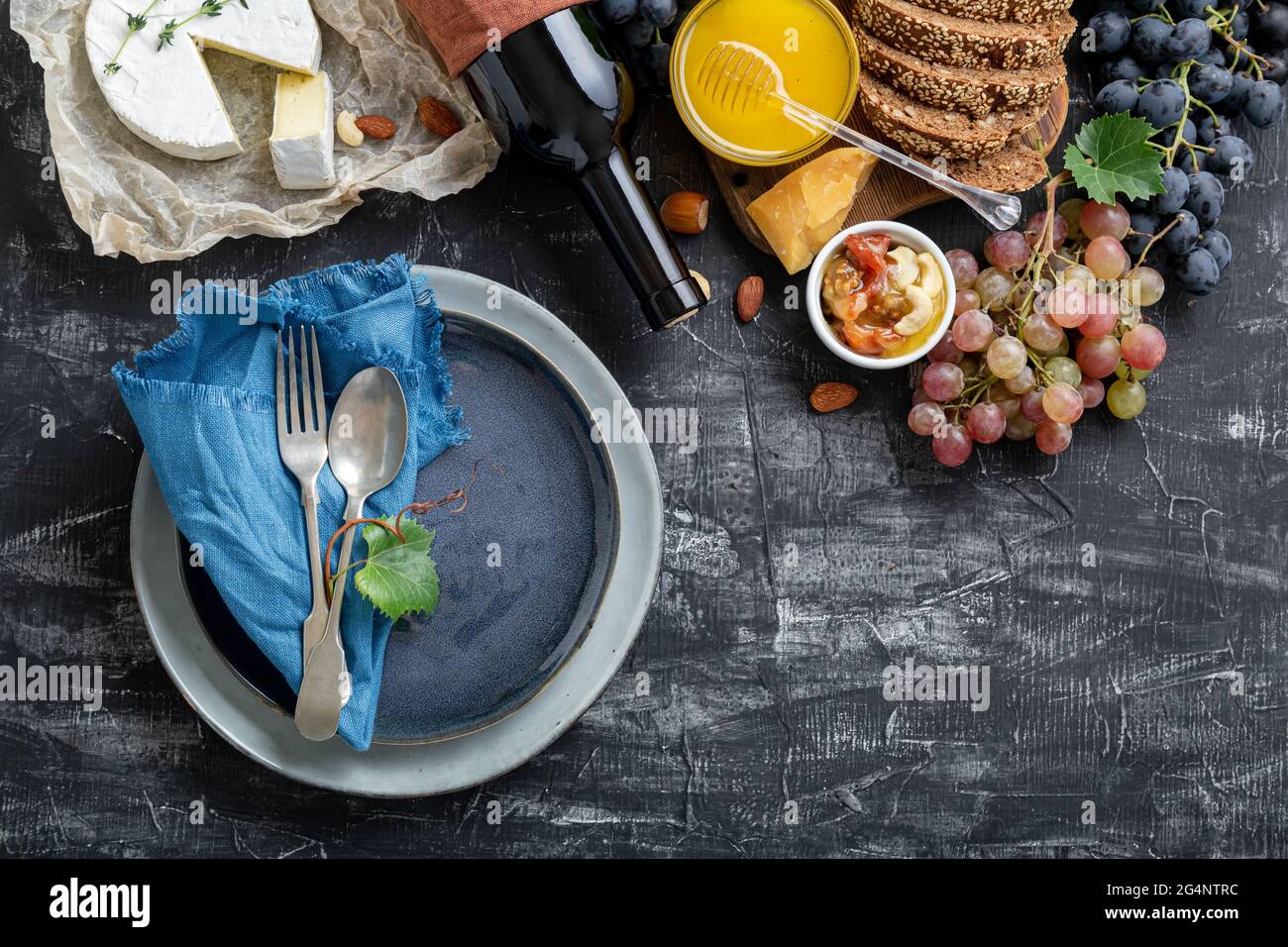 Leere Portion blauen Teller mit Gabellöffel in Rahmen von Lebensmitteln Zutaten mediterrane Küche. Blauer Teller im Rahmen von Essen, Wein, Käse auf dunkel Stockfoto