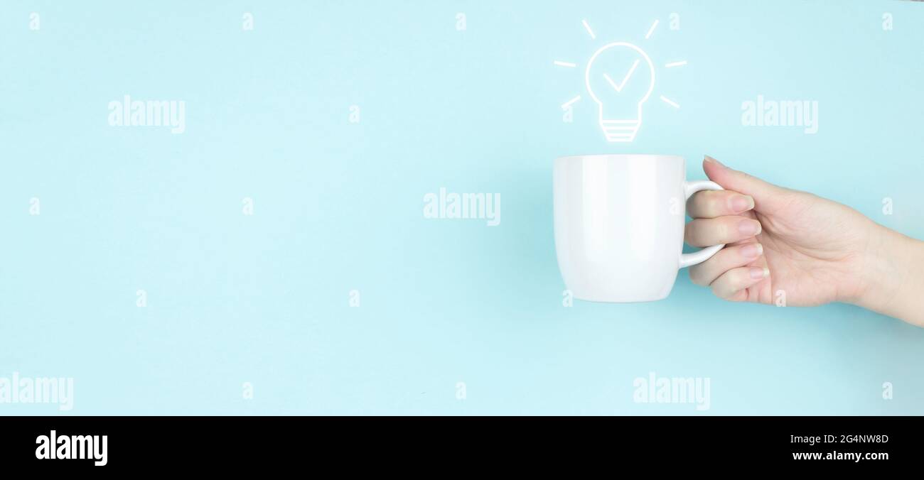 Unternehmensstart oder Ziel zum Erfolg. Mädchen Hand halten Morgen Kaffeetasse mit Licht Bulp Zeichen Symbol auf blauem Hintergrund. Lösungsanalyse und -Entwicklung Stockfoto