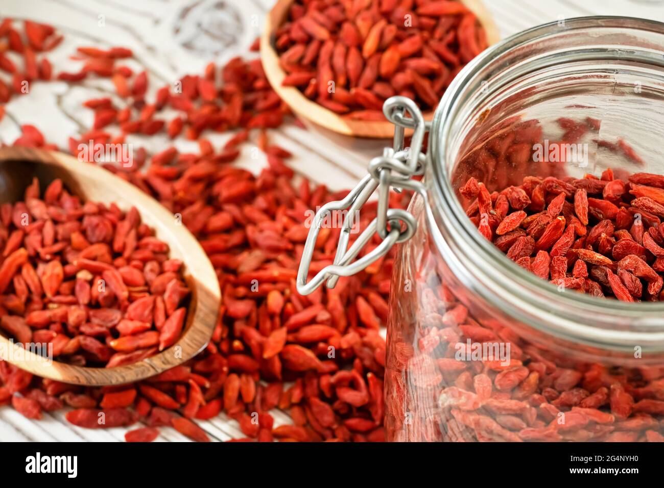 Getrocknete Goji aka. wolfberry Samen in Glasflasche, einige mehr verschwommen in Holzschüsseln und verschüttet auf weißen Brettern Schreibtisch Stockfoto