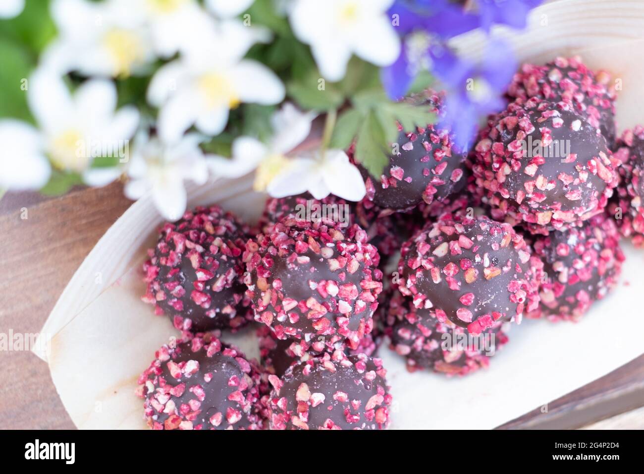 Schachtel Pralinen mit roten Nüssen auf einem Holztisch mit Blumen. Muttertag oder Valentinstag Feier. Stockfoto