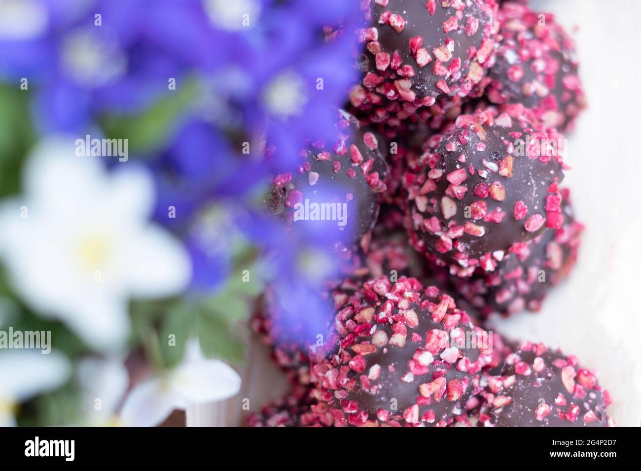 Schachtel Pralinen mit roten Nüssen auf einem Holztisch mit Blumen. Muttertag oder Valentinstag Feier. Stockfoto