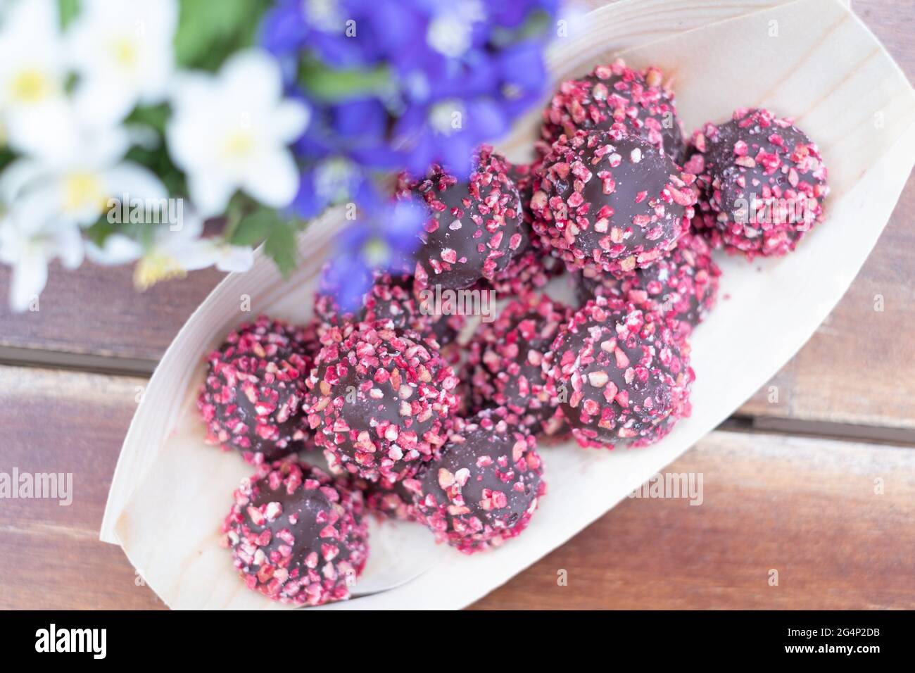 Schachtel Pralinen mit roten Nüssen auf einem Holztisch mit Blumen. Muttertag oder Valentinstag Feier. Stockfoto