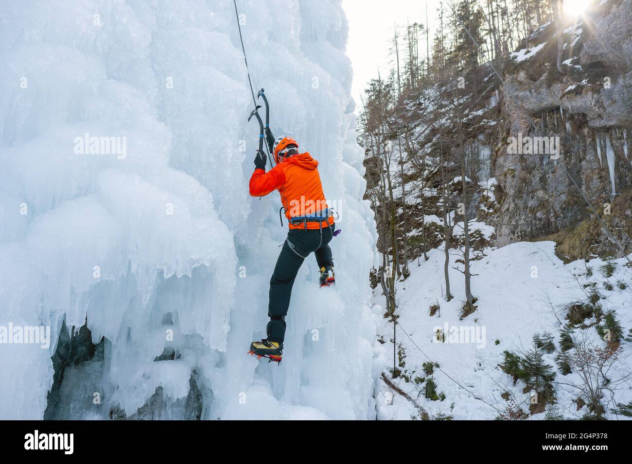 Athlet klettern gefrorenen Wasserfall, schwingen die Axt Pick in das Eis und verwenden es als Griff, um sich nach oben zu ziehen Stockfoto