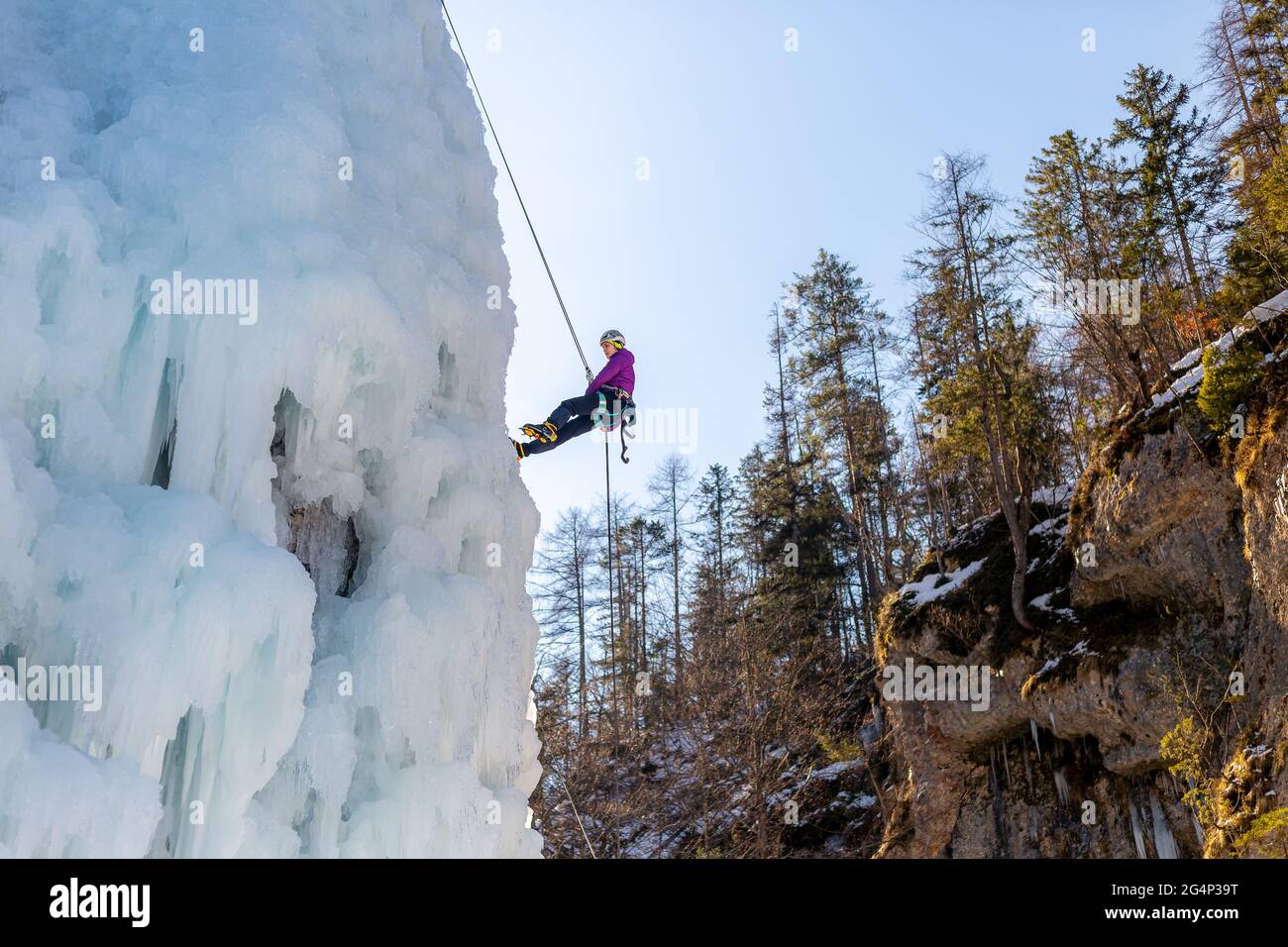 Frau klettert auf einem gefrorenen Wasserfall in Technik nach vorne gerichtet mit einem Fuß und flach mit dem anderen Stockfoto