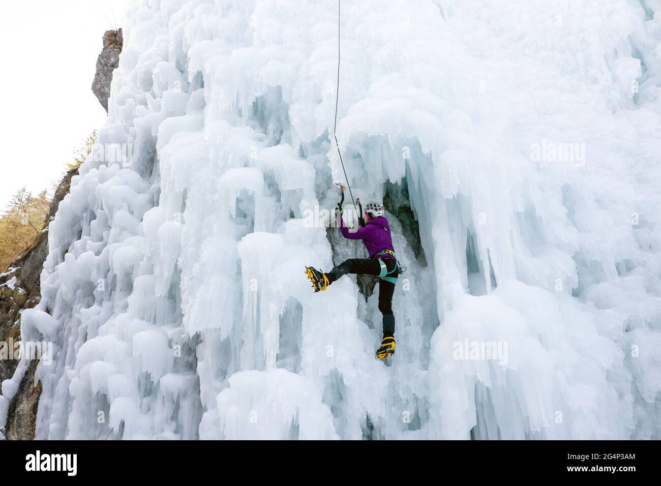 Alpinistin mit Eiskletterausrüstung, Axt und Kletterseilen, Klettern an einem gefrorenen Wasserfall, Blick von unten Stockfoto