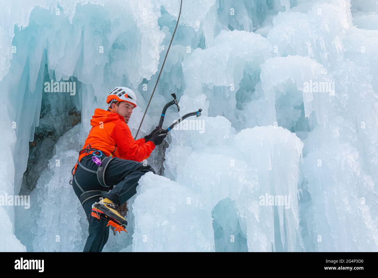 Athlet klettern gefrorenen Wasserfall, schwingen die Axt Pick in das Eis und verwenden es als Griff, um sich nach oben zu ziehen Stockfoto