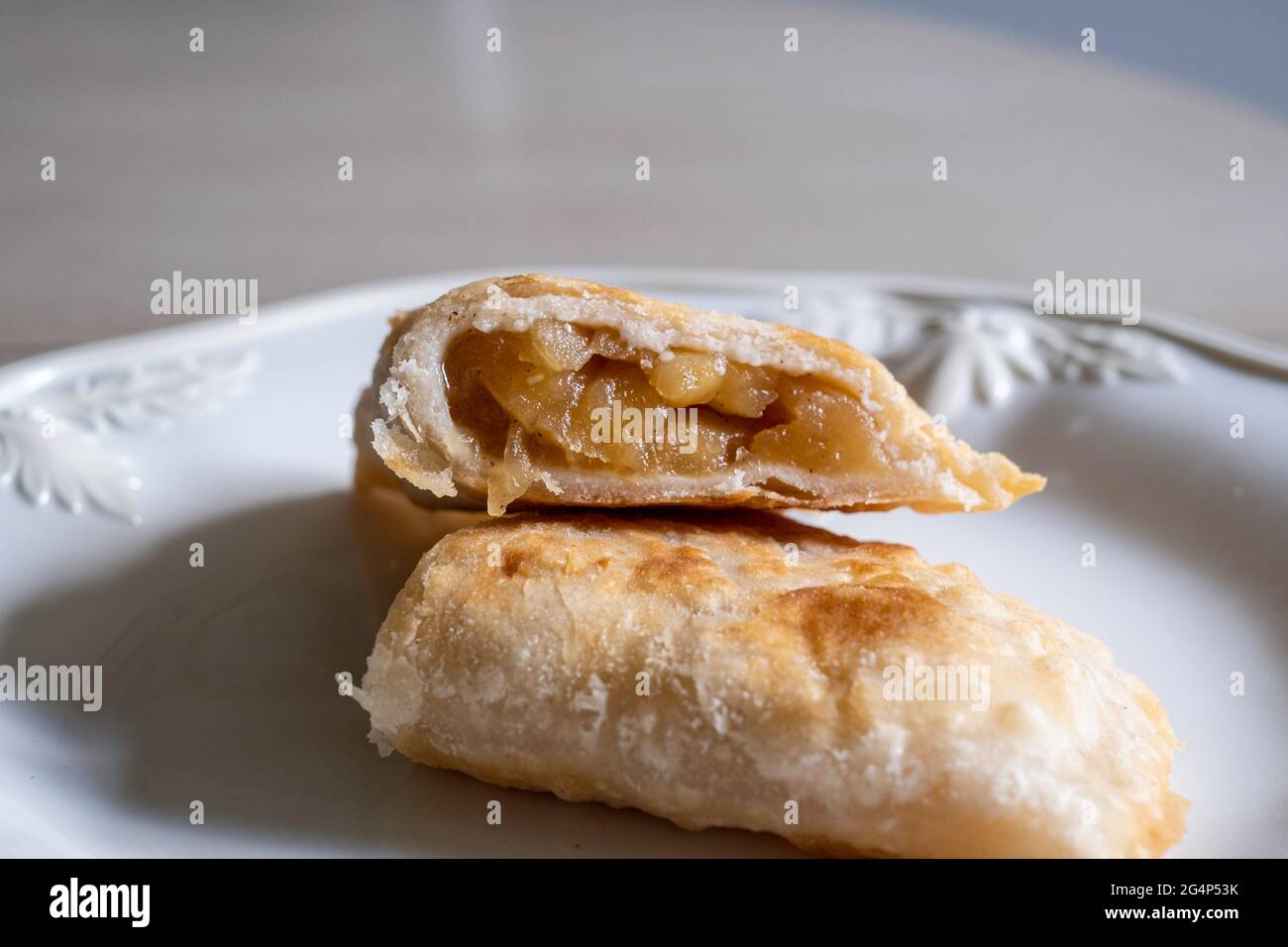 Hausgemachter gebratener Apfelkuchen, halbiert aus getrockneten Äpfeln mit schuppiger Kuchenkruste auf einem weißen Teller. Stockfoto