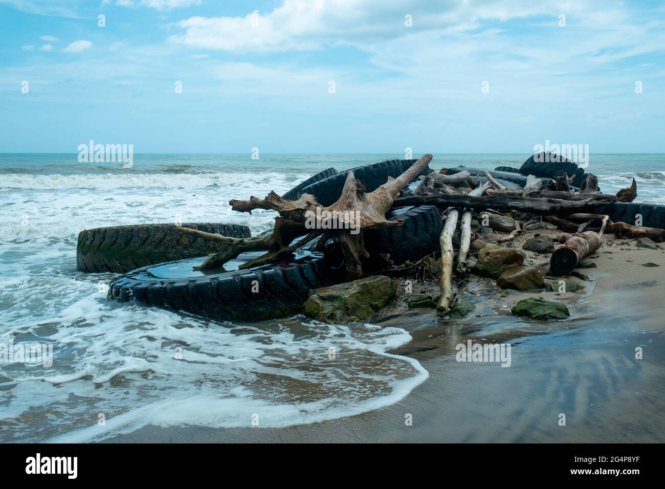 Riesige Reifen von Heavy Machinery zusammen mit riesigen Baumstämmen und Steinen am Ufer des Strandes, um die Kraft der Wellen zu schneiden Stockfoto