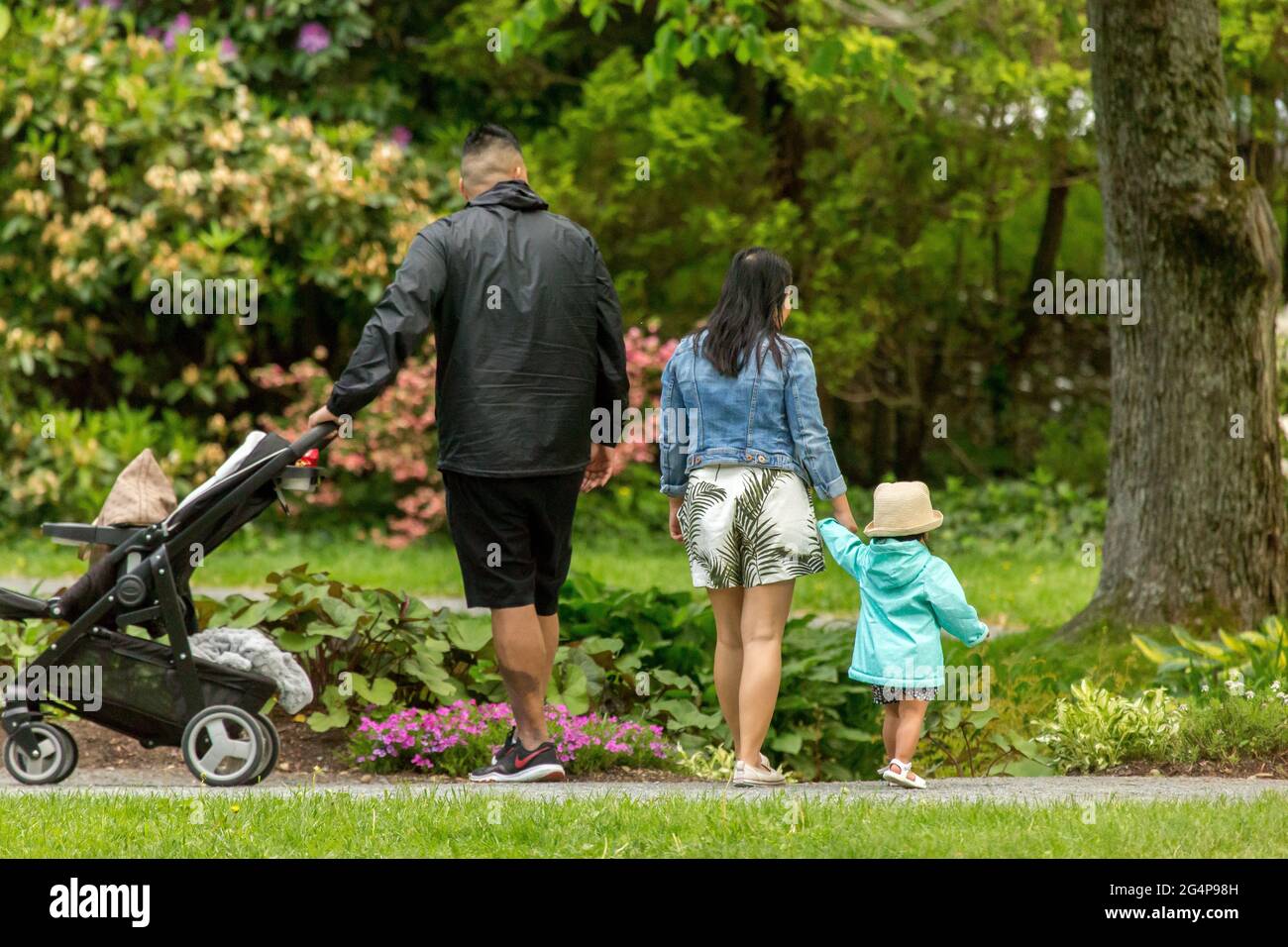 Ein junges Paar mit Tochter, das in einem öffentlichen Park mit dichtem Grün spazierengeht. Stockfoto