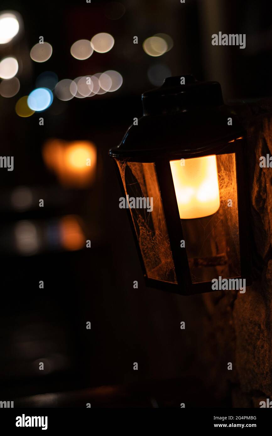 Düstere Straßenlaterne, die mitten in der dunklen Nacht mit einem orangefarbenen Licht beleuchtet wird, mit einem Hintergrund aus unscharf abstrahlenden Lichtern, vertikalem Bokeh Stockfoto
