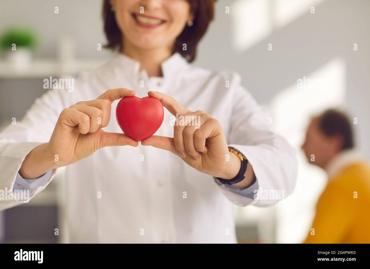 Nahaufnahme eines kleinen roten Herzens, das in den Händen einer lächelnden Kardiologin gehalten wird. Stockfoto