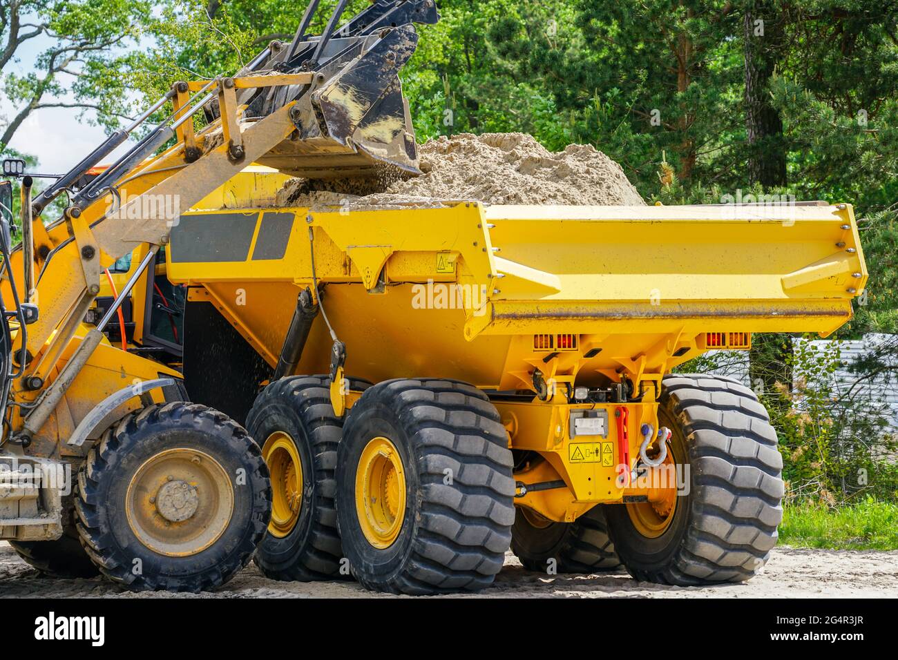 Gelber Frontlader lädt den Sand in den Muldenkipper Stockfoto